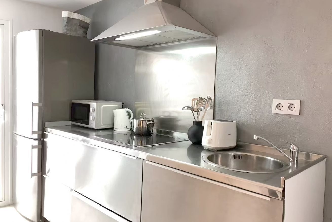 Una cocina moderna con electrodomésticos de acero inoxidable, microondas, hervidor, tostadora y un lavabo.
