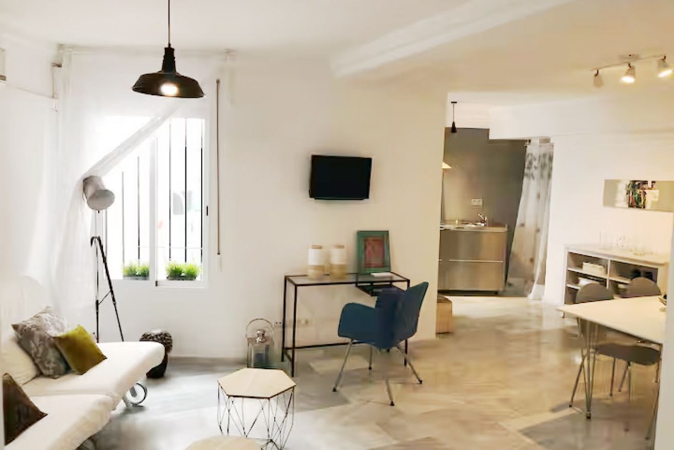 Una sala de estar moderna con un sofá, una mesa de comedor, un televisor y una zona de cocina al fondo.