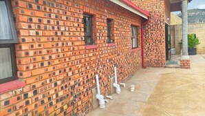 A red brick building with a red roof, a door, and windows. There are pipes and a plant on the ground. - Lethabo Mountain View Guest House Cheap  (Maluti a Phofung)