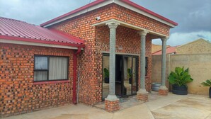 A two-story brick house with a red roof, a covered porch with columns, and a paved patio area. - Lethabo Mountain View Guest House Cheap  (Maluti a Phofung)