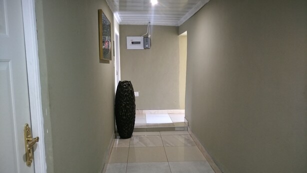 A hallway with a tiled floor, a door with a brass handle, a wall-mounted air conditioning unit, and a black vase. - Lethabo Mountain View Guest House Cheap  (Maluti a Phofung)