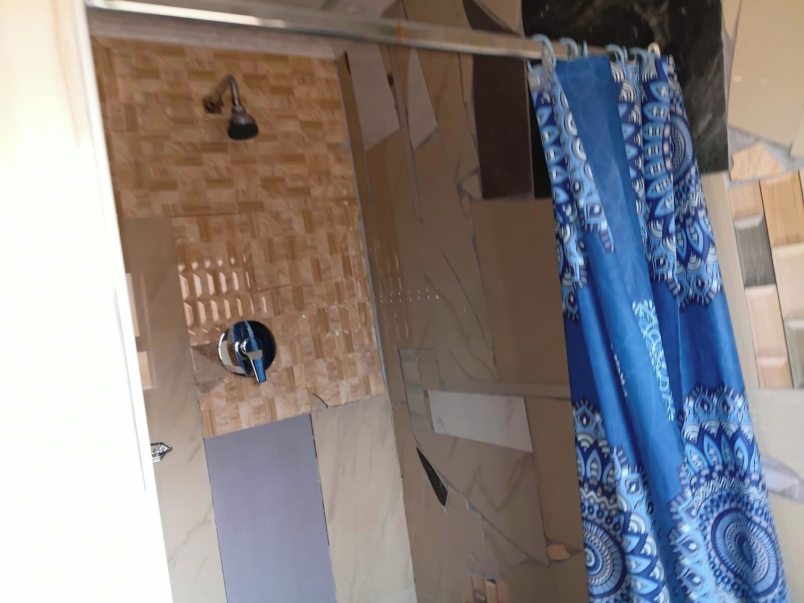 A shower area with a patterned curtain, a handheld showerhead, and a tiled wall.