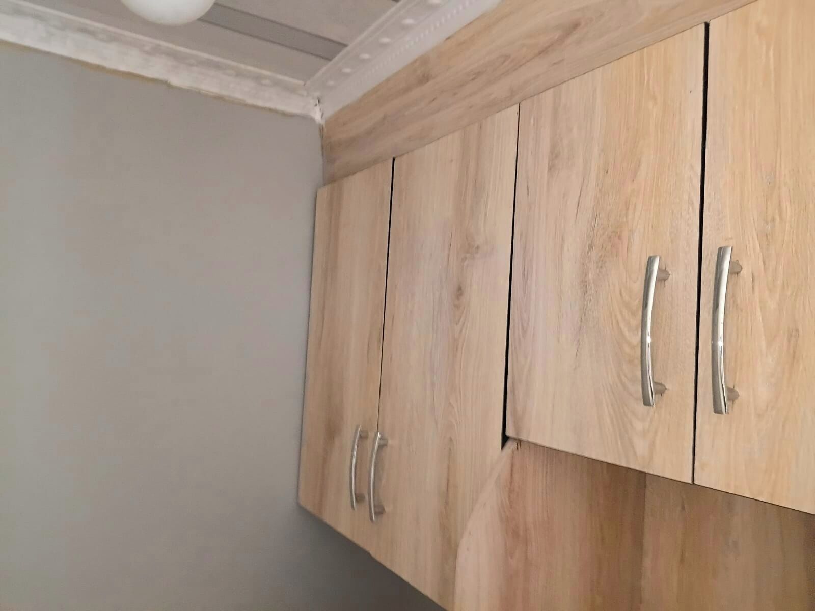 Un mueble de madera con dos tiradores, un techo con moldura decorativa blanca y una pared lisa.