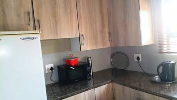 Une cuisine avec des meubles de rangement en bois, un réfrigérateur blanc, un four à micro-ondes, une bouilloire et une assiette ronde posée sur le plan de travail.