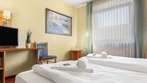 Hotelkamer met een bed, bureau met televisie, stoel, schilderij en raam met gordijnen.