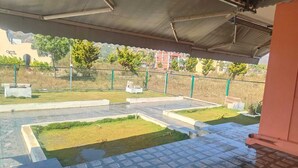 A covered outdoor area with tiled flooring, concrete planters, and a green fence.