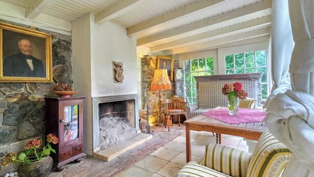 A room with a stone fireplace, a wooden cabinet, a sofa, and a table with a vase of flowers. - house DEV (Maribor)