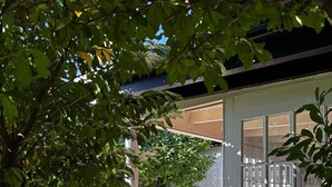 A covered patio area with a table and chairs, surrounded by greenery and a view of the street. - house DEV (Maribor)