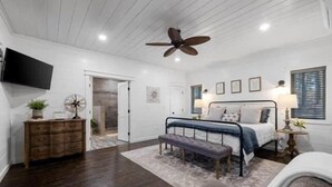 Ein Schlafzimmer mit Bett, Sitzbank, Kommode, Deckenventilator und Fernseher.