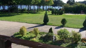 A well-maintained lawn with a swing set, a small garden area with shrubs, and a view of a body of water. - Mobile Home im Ferienpark mit Seezugang (Dabel)