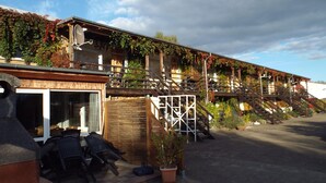 A building with a wooden facade, outdoor seating, and a staircase leading to a balcony. - Mobile Home im Ferienpark mit Seezugang (Dabel)