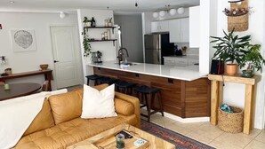 A modern living room with a brown leather sofa, a wooden coffee table, and a kitchen with white cabinets and a central island. - Breckenridge 1BR + Den - Family-Friendly, Steps to Swan River & CO Trail (Breckenridge)