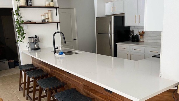 A modern kitchen with a white countertop, stainless steel appliances, and wooden stools. - Breckenridge 1BR + Den - Family-Friendly, Steps to Swan River & CO Trail (Breckenridge)