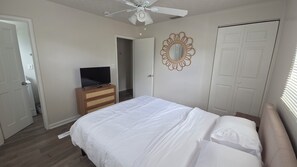 A bedroom with a bed, a television on a dresser, a ceiling fan, and a door.