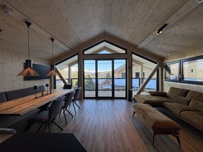 A spacious room with a wooden ceiling, a large dining table, a sofa, and a view of mountains through large windows. - Superior Chalet in Turrach With Sauna (Stadl-Predlitz)