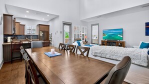 Een moderne keuken met houten kastjes, een eethoek met een houten tafel en stoelen, een gezellige zithoek met een zachte, witte plaid, en een grote flatscreen televisie.