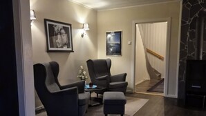 Un salon doté d’un parquet en bois foncé, d’une cheminée en pierre, de deux fauteuils, d’une table basse et d’un éclairage mural.