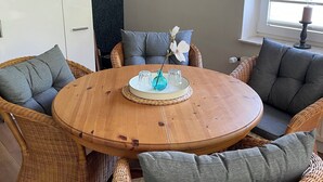 A round wooden table with a woven placemat, surrounded by wicker chairs with grey cushions. A modern pendant light hangs above. - Seeperle by the Lake Vacation Rental (Lalendorf)