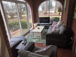 Ein gemütliches Wohnzimmer mit Fernseher, Rattanmöbeln und Blick auf die Straße.