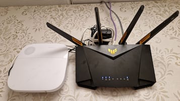 A white device connected to a black router with multiple antennas on a patterned fabric surface.