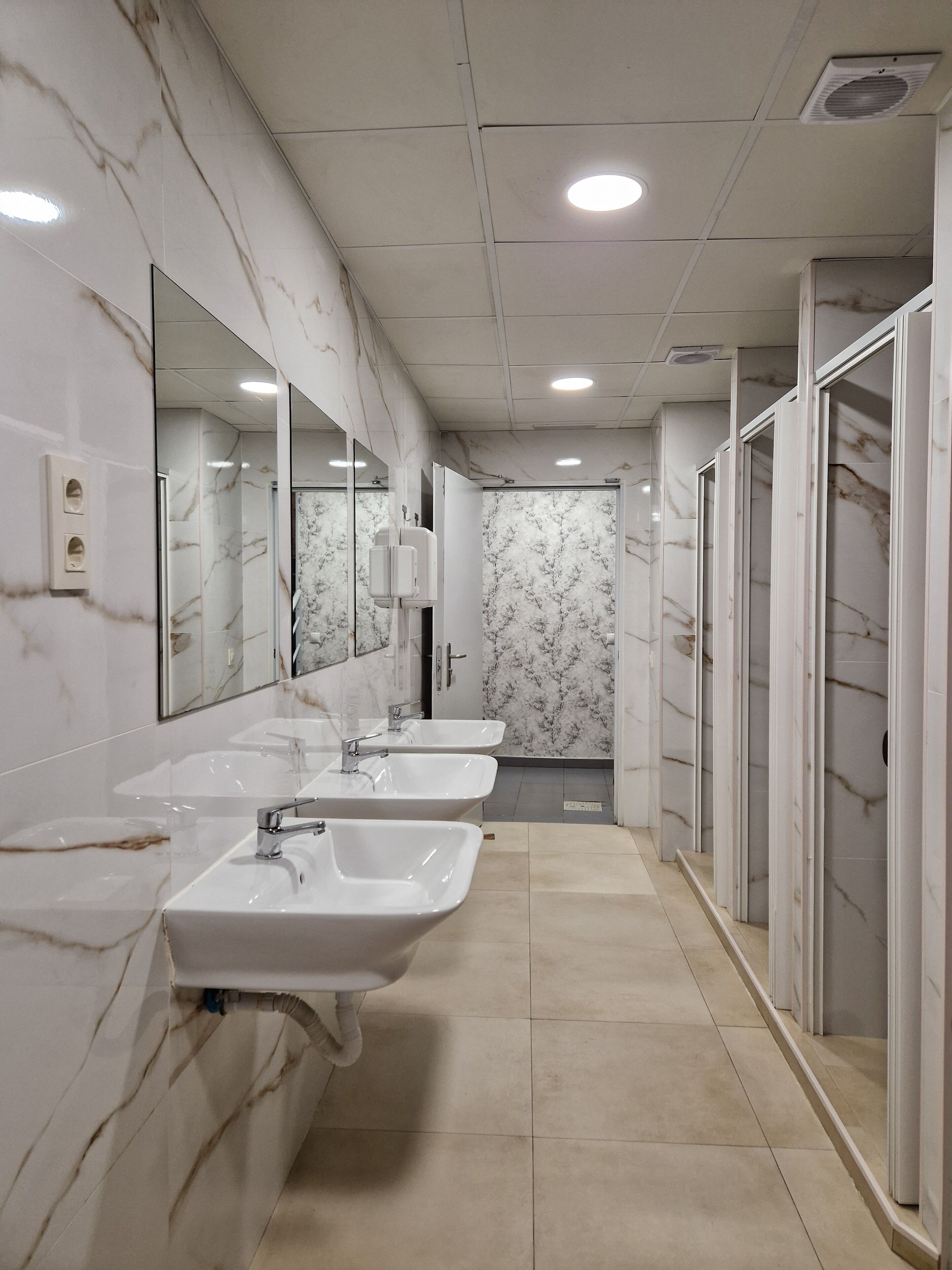 A bathroom with three sinks, a mirror, and a shower area.