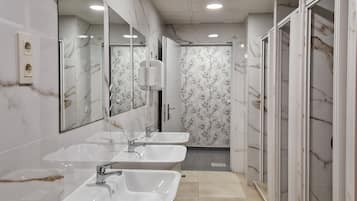 Un baño con tres lavamanos, un espejo y una zona de ducha.