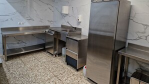 A commercial kitchen with stainless steel appliances, marble walls, and a tiled floor. - PALOMERAS Coliving & Coworking (Madrid)