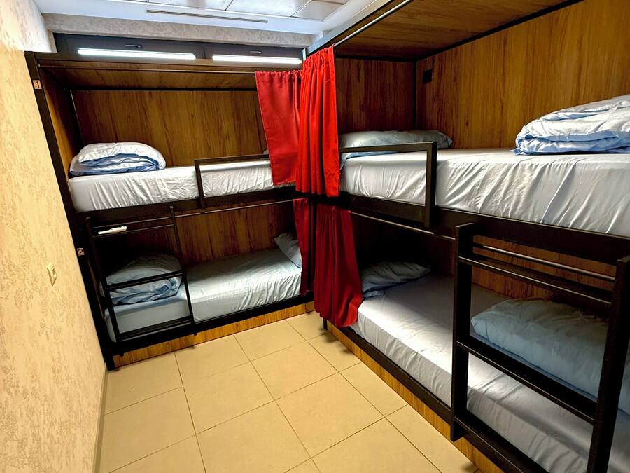 A compact, single-room accommodation with bunk beds, a red curtain, and a skylight.