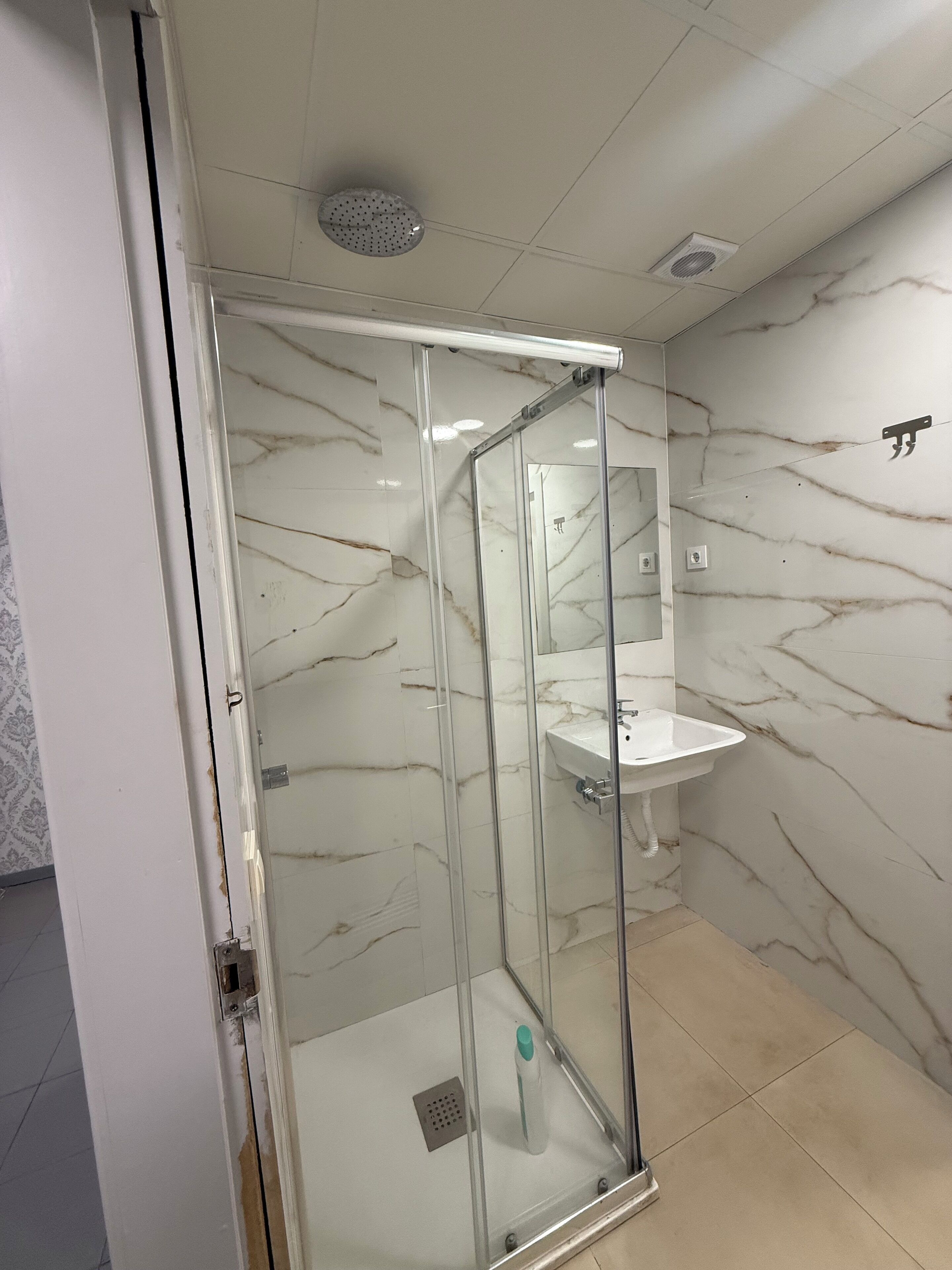 A glass-enclosed shower with a white sink and marble walls.