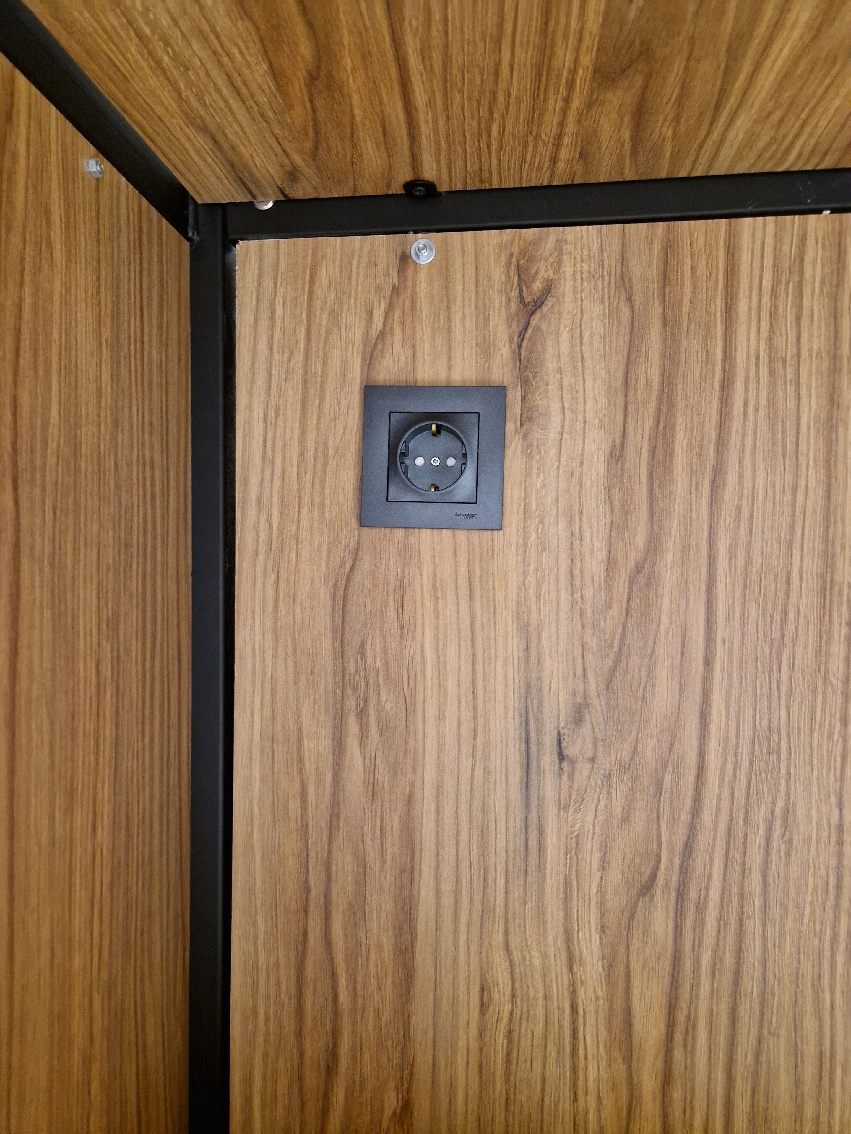 Eine Holzwand mit schwarzem Metallrahmen und einer rechteckigen Steckdose.
