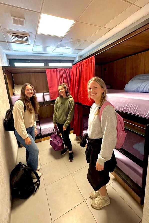 Une chambre de dortoir avec des lits superposés, un rideau rouge et un sol carrelé.