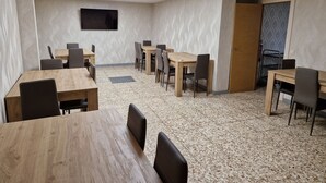 A conference room with wooden tables and chairs, a flat-screen TV mounted on the wall, and a patterned floor. - PALOMERAS Coliving & Coworking (Madrid)