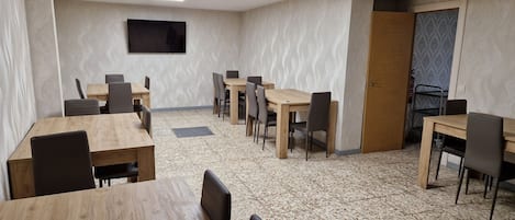 Un salón de conferencias con mesas y sillas de madera, un televisor de pantalla plana en la pared y un suelo con diseño.