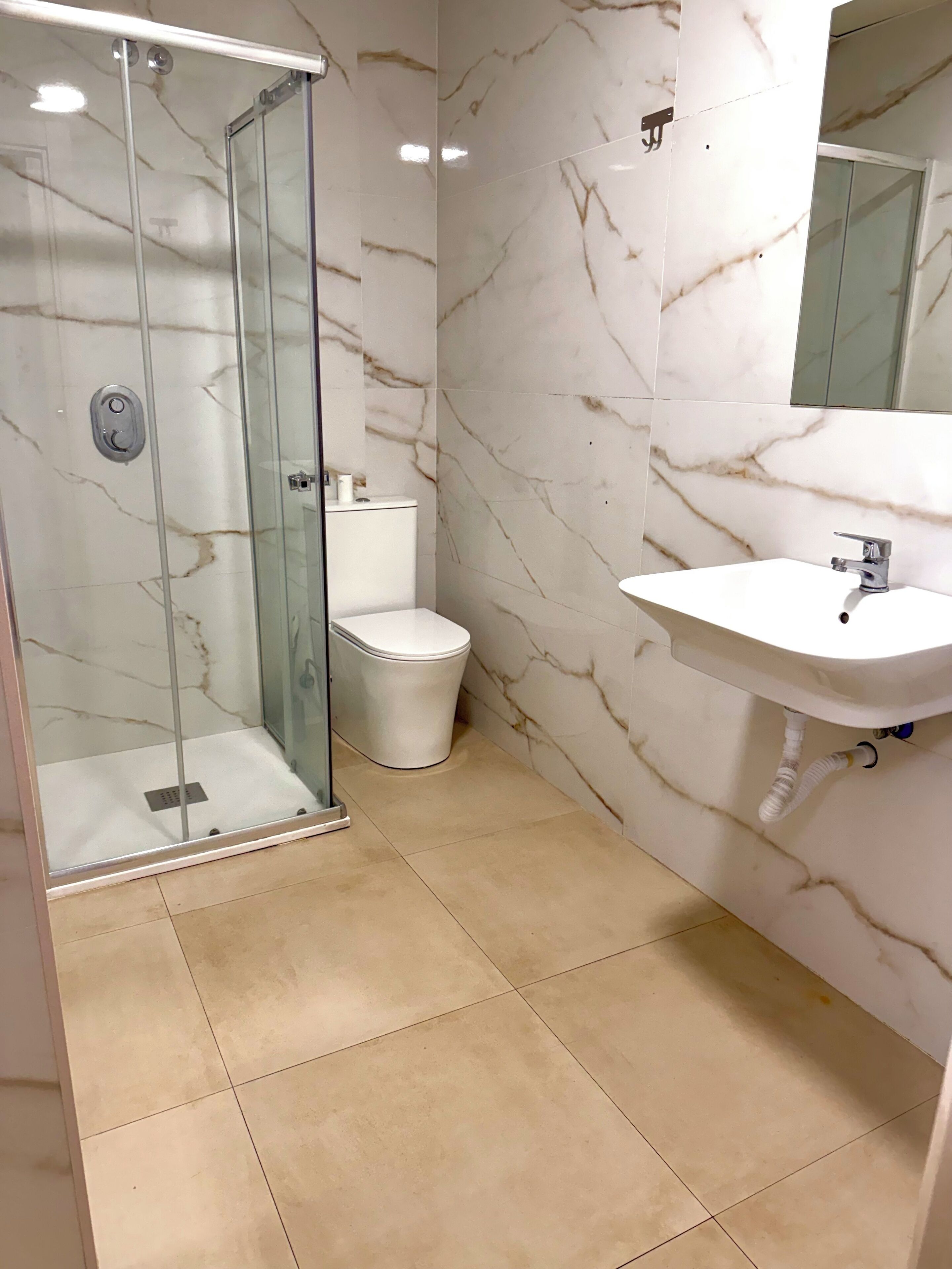 A bathroom with a glass-enclosed shower, a toilet, and a sink.
