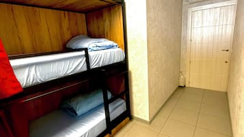 Una habitación con literas, piso de baldosas, una puerta e iluminación empotrada en el techo.