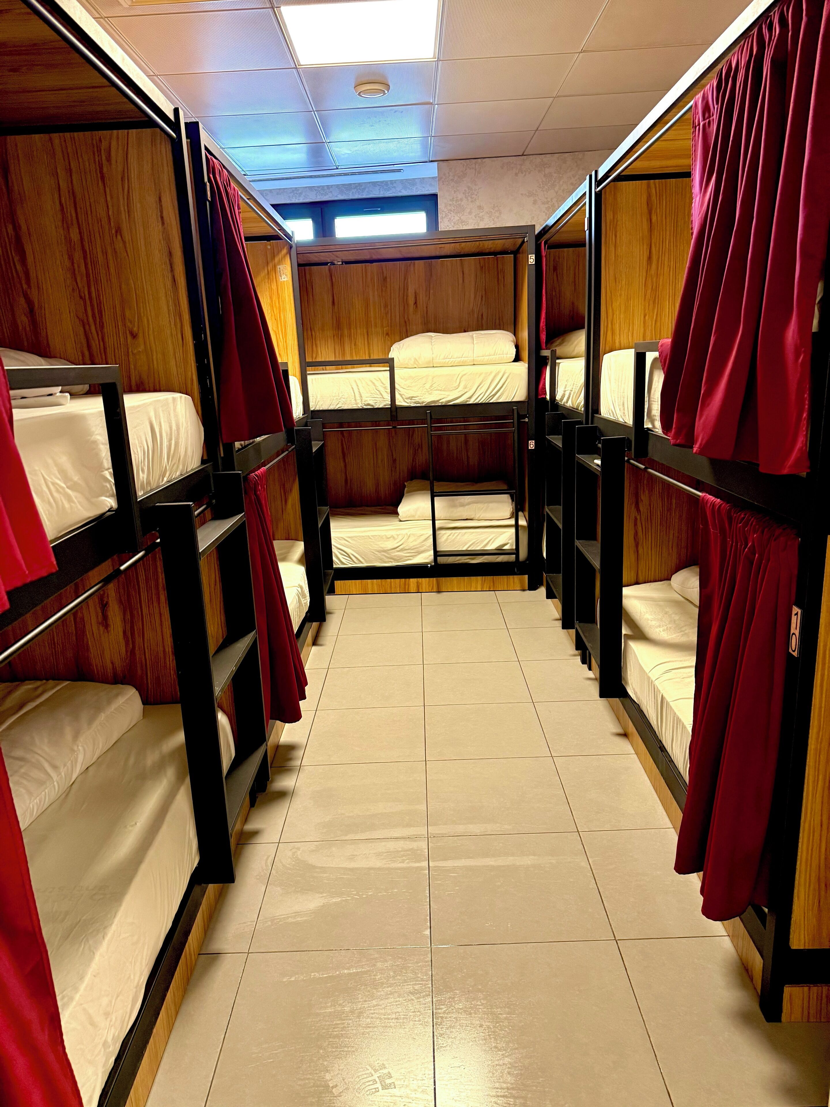 Um corredor com beliches, paredes de madeira e cortinas vermelhas.