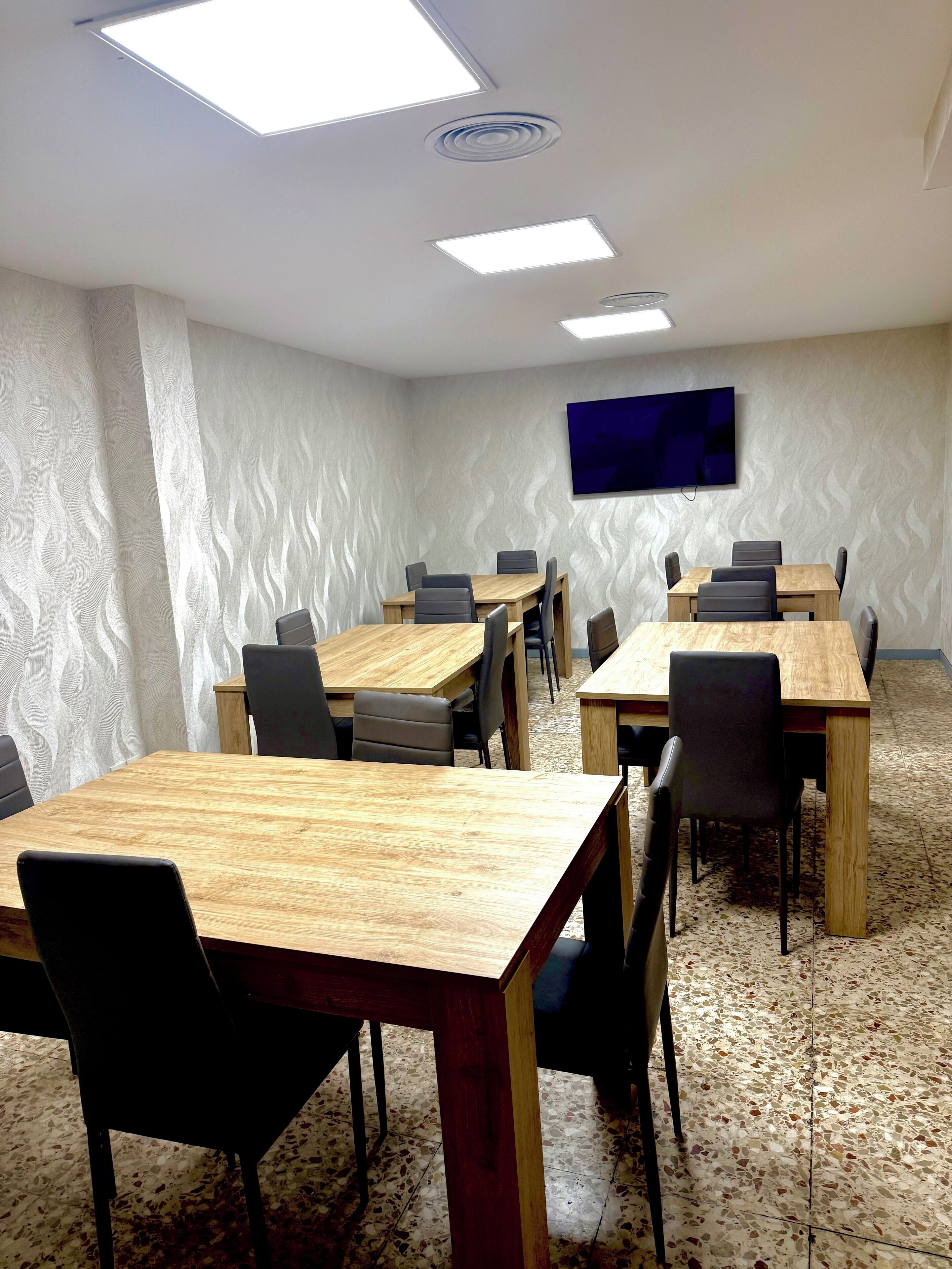 A conference room with wooden tables and chairs, a flat-screen TV mounted on the wall, and a patterned floor.