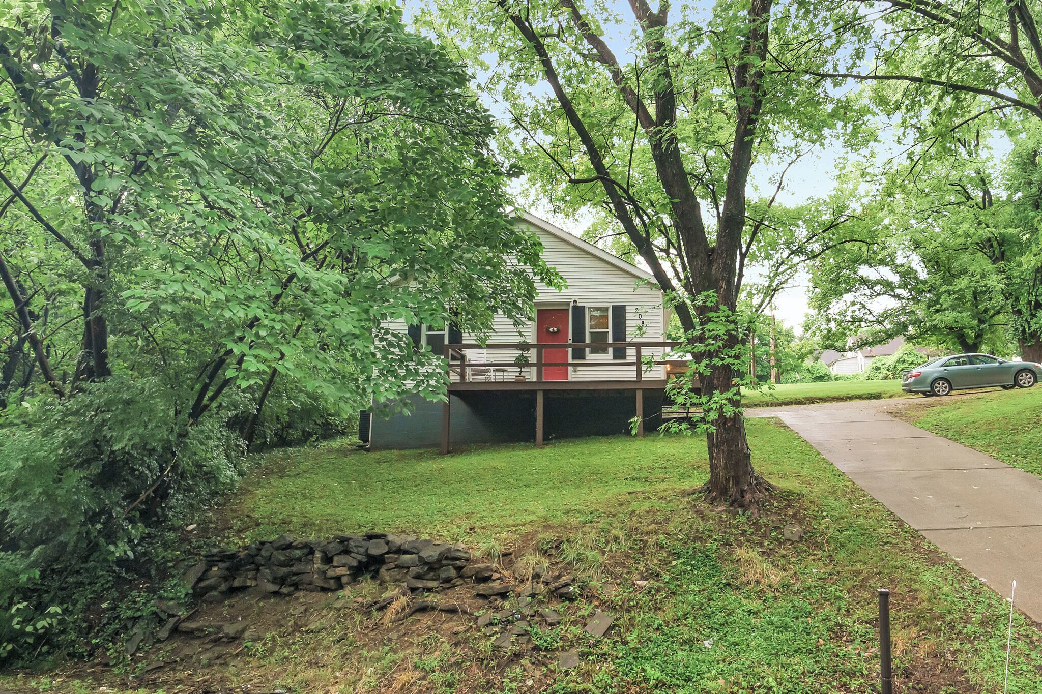 A single-story house with a red door, surrounded by trees and a grassy yard.