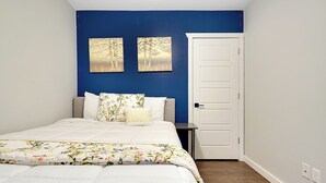 Ein Schlafzimmer mit einem Bett, einem Nachttisch, einer Tür und zwei an der Wand hängenden Bildern.