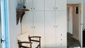 Ein Zimmer mit einem Bett, einem Sessel, einem Schreibtisch, einem weißen Kleiderschrank und einem Regal mit einem Gerät.