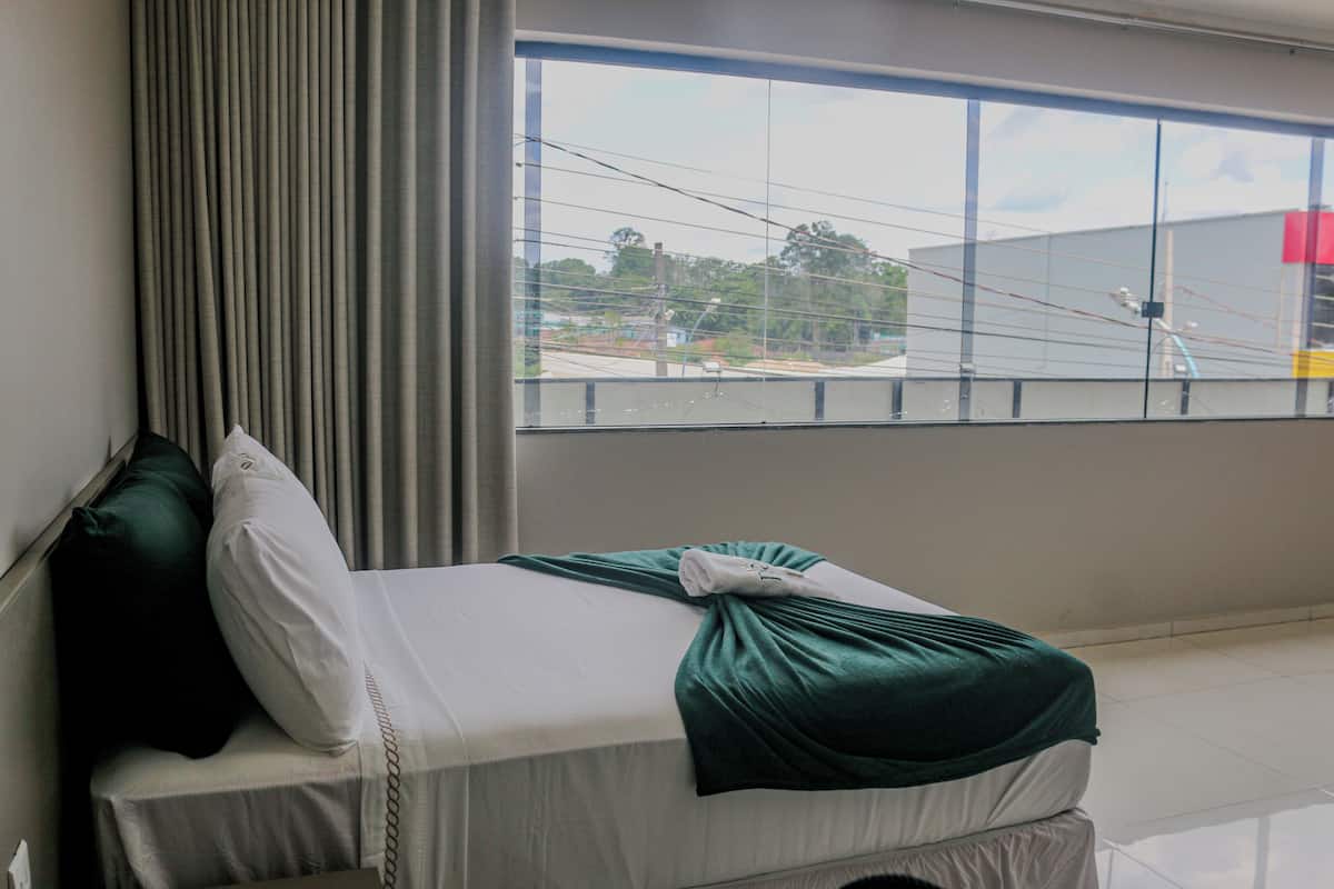 A hotel room with a bed, curtains, and a large window with a view of the outside.