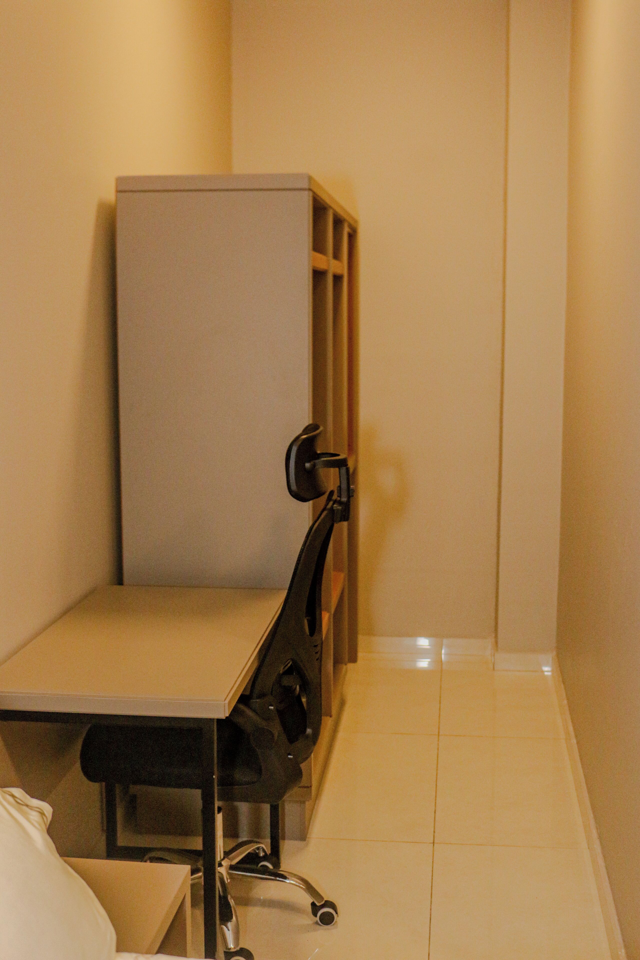 A narrow corridor with a cubicle-style desk and a chair, a metal desk lamp, and a tiled floor.