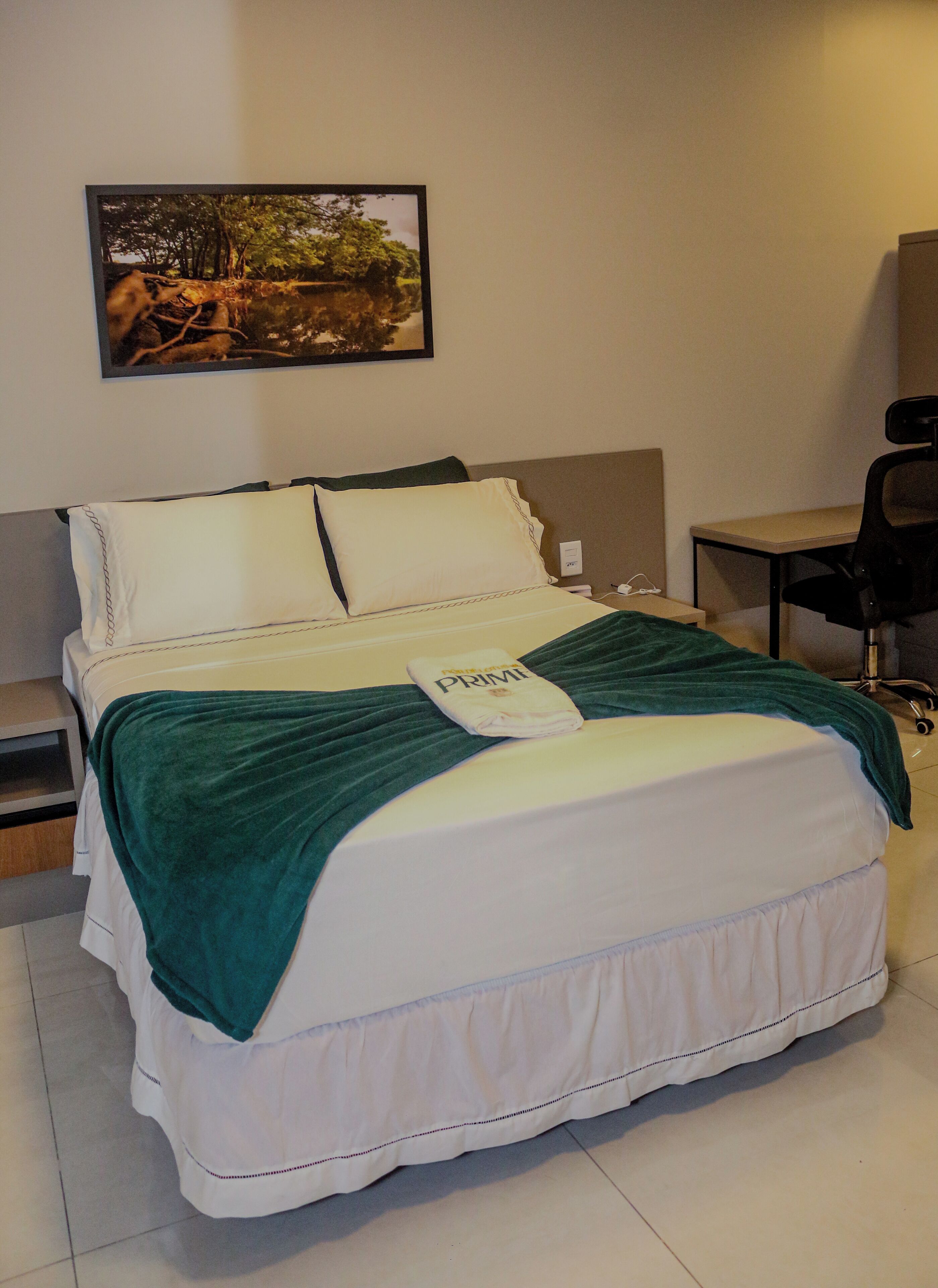 A bed with a green blanket, white pillows, and a framed picture on the wall.