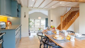 Un comedor con una mesa de madera dispuesta para una comida, una cocina con armarios azules y una escalera.