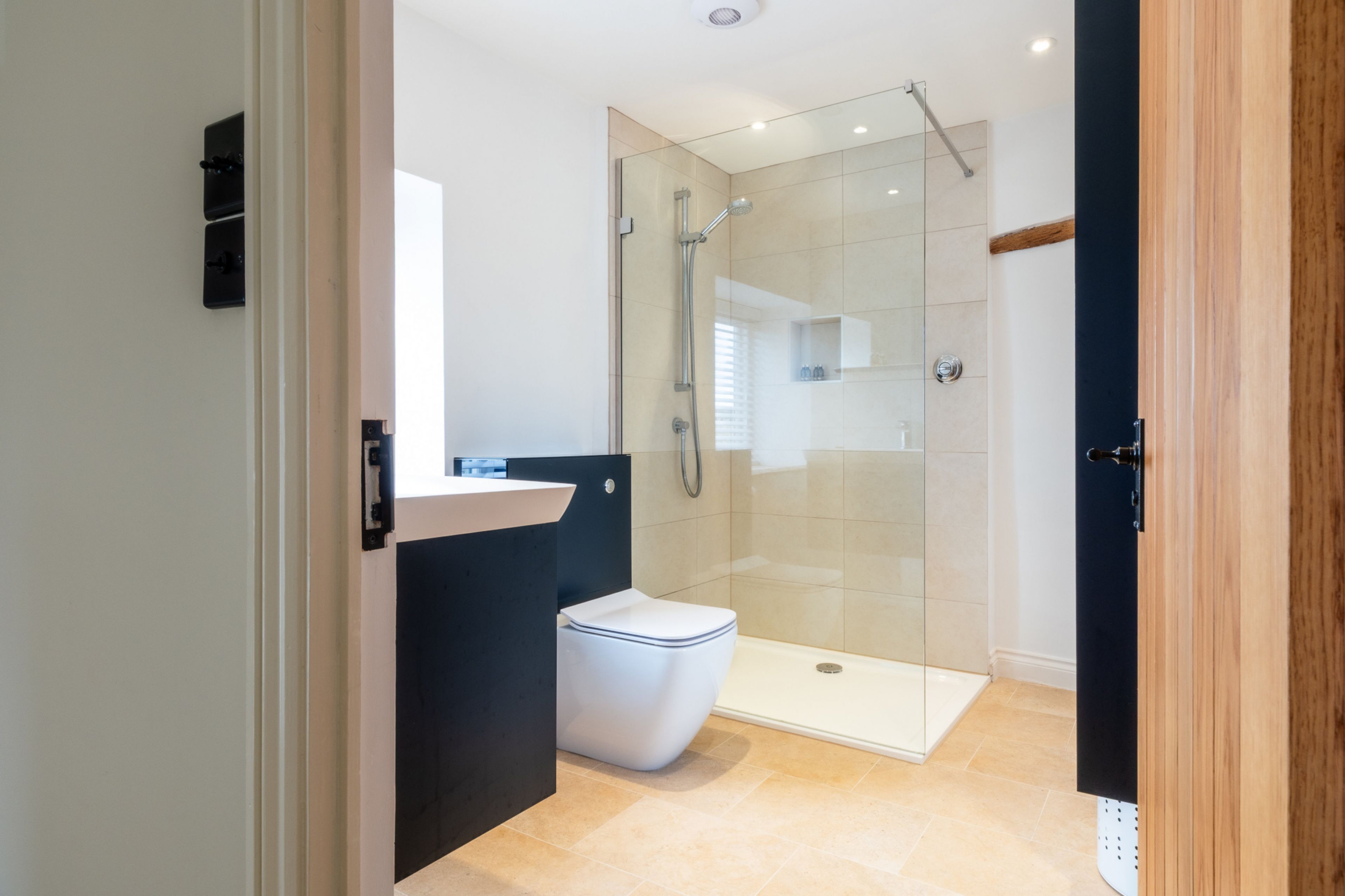 Et moderne badeværelse med et glasafskærmet brusebad, et hvidt toilet og en sort vask.