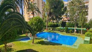 Una piscina rodeada de césped, árboles y un edificio al fondo.