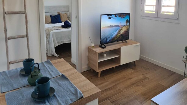 Una habitación con una cama, un televisor sobre un soporte de madera, una escalera y una mesa con tazas.
