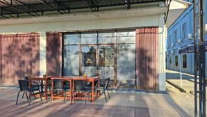 An outdoor seating area with a wooden table and chairs, a glass door entrance, and a blue building in the background. - ACO BORNEO HOTEL (Malinau)