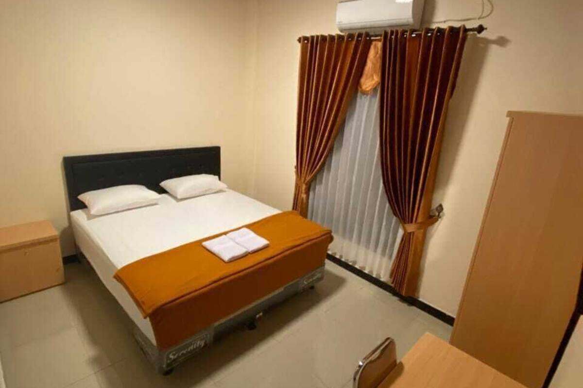 A hotel room with a bed, an air conditioning unit, curtains, a wooden desk, and a wardrobe.