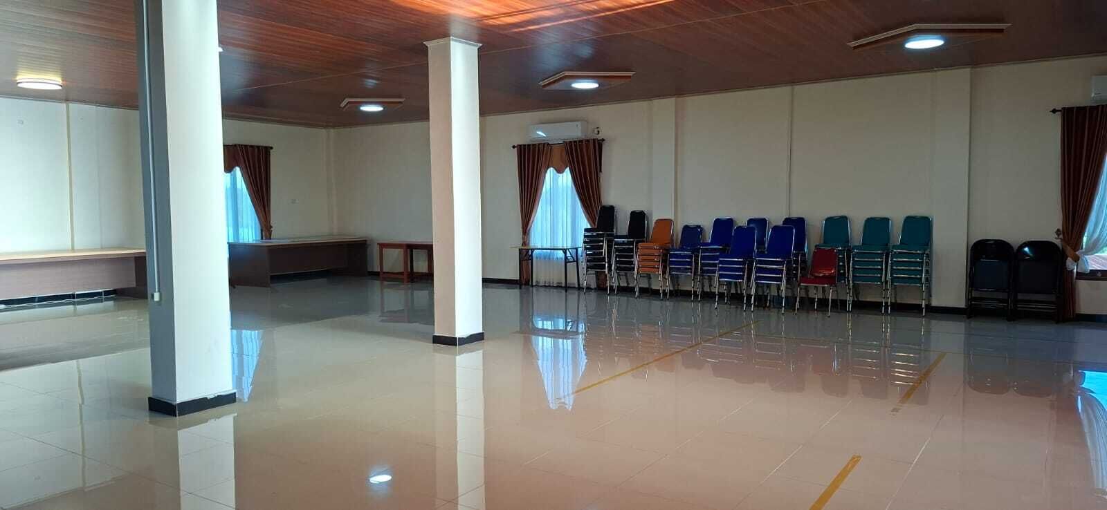 Ein geräumiger Saal mit glänzendem Boden, Stuhlreihen und einer hohen Decke mit eingelassenen Leuchten.